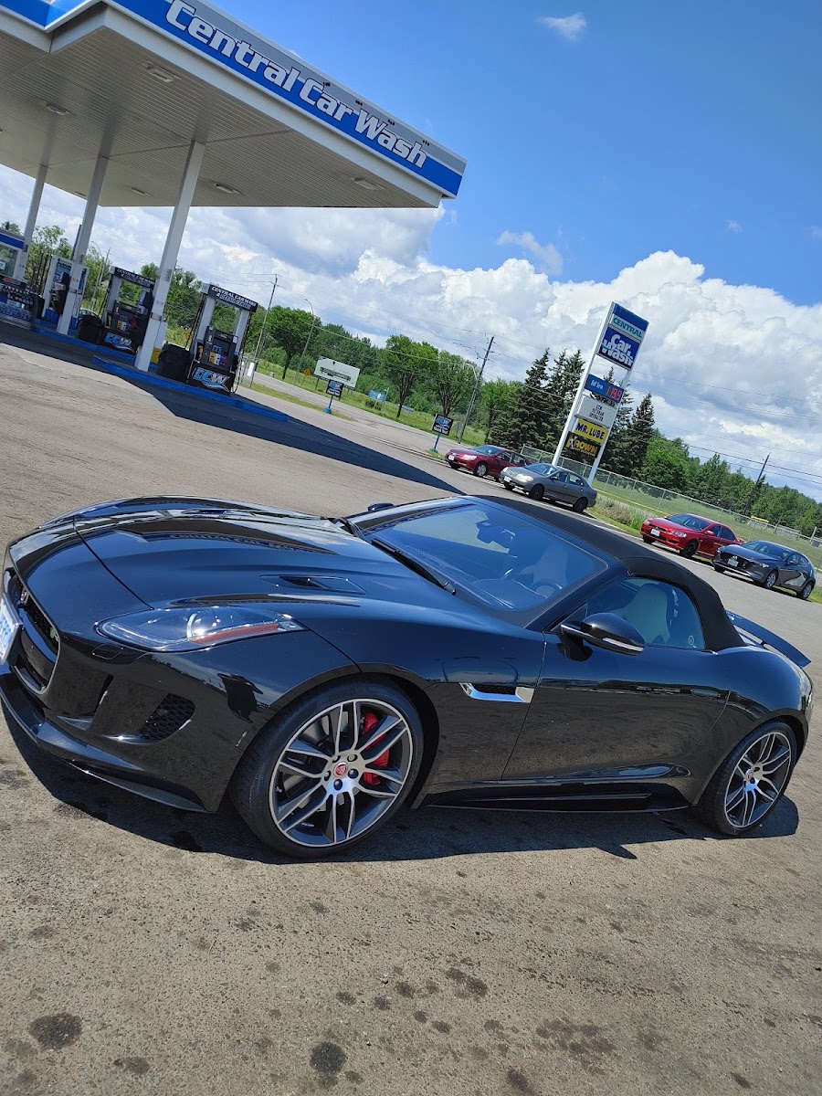 Glossy black Jaguar at Central Car Wash with canopy and Thunder Fuels pumps behind it.